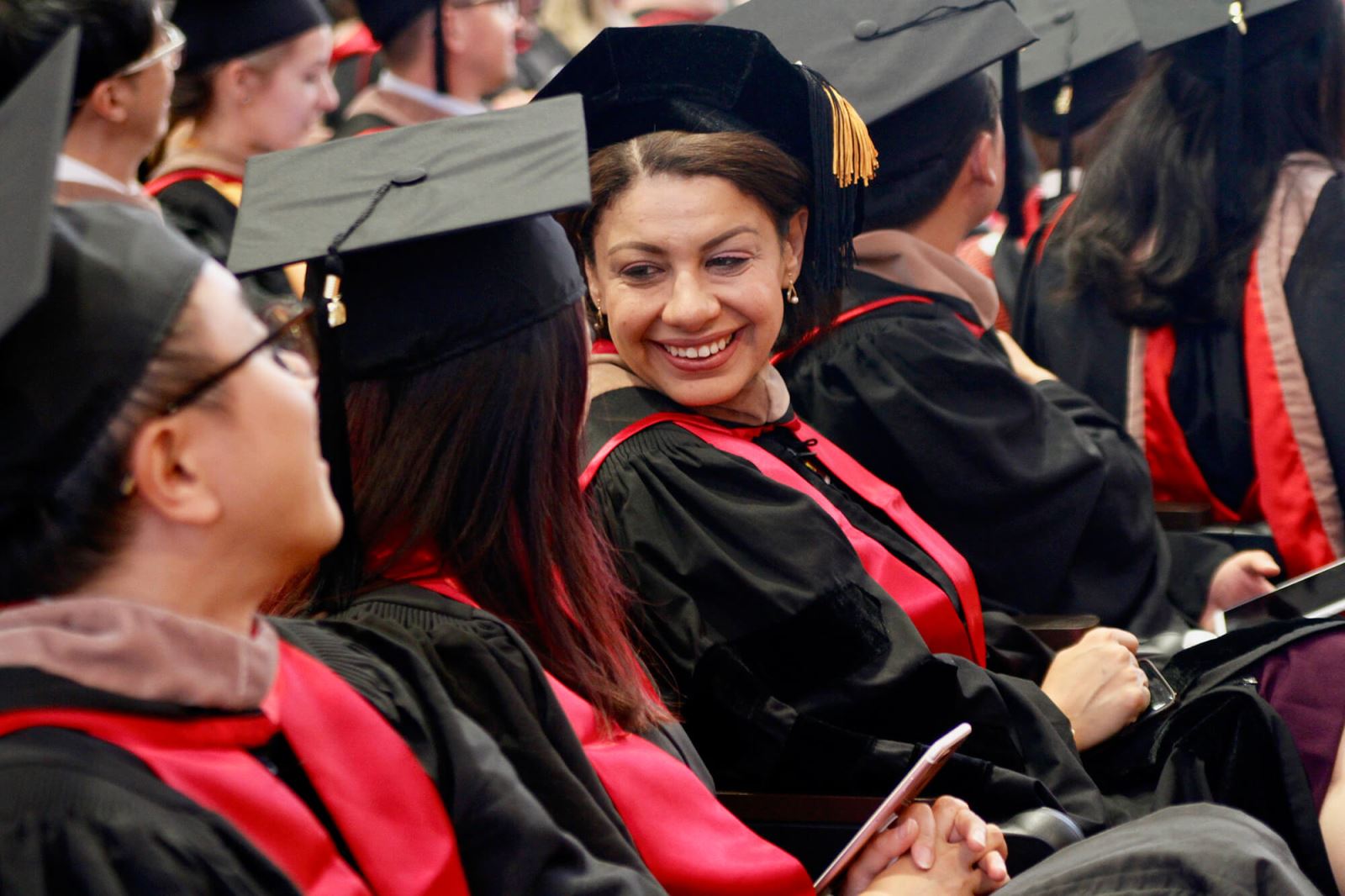 Stanford GSB graduates in caps and gowns smiling.