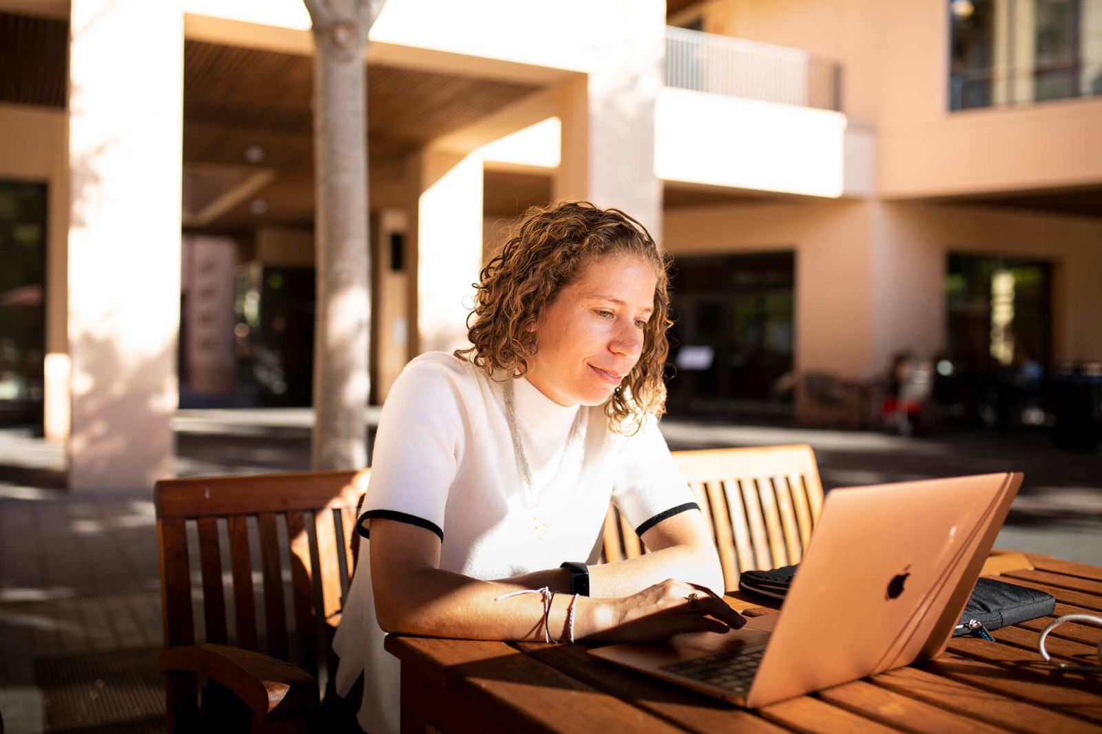 Woman working at picnic table with laptop. 