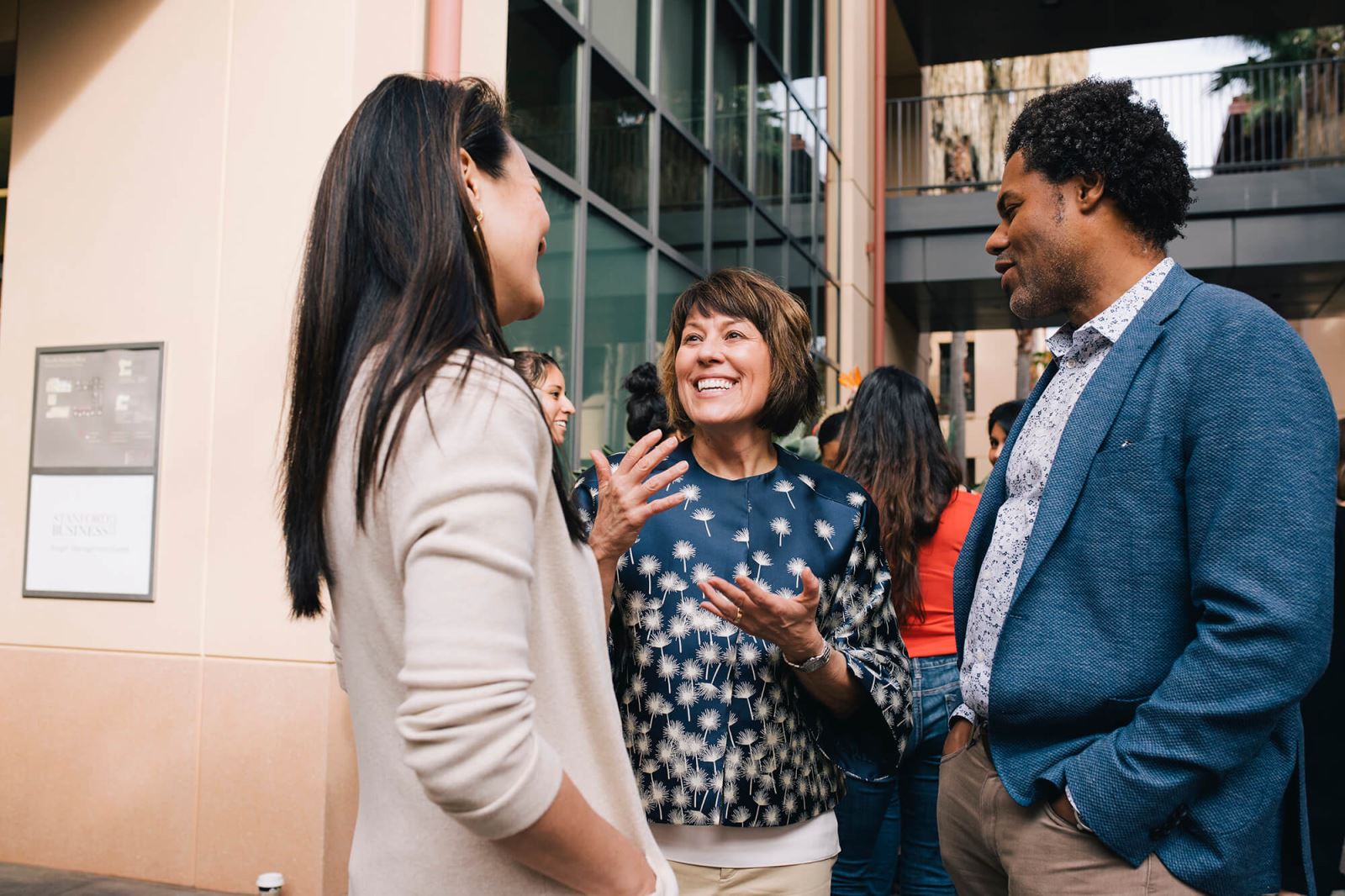 Two female and one male student in business attire engage in lively discussion outside of Stanford classroom.