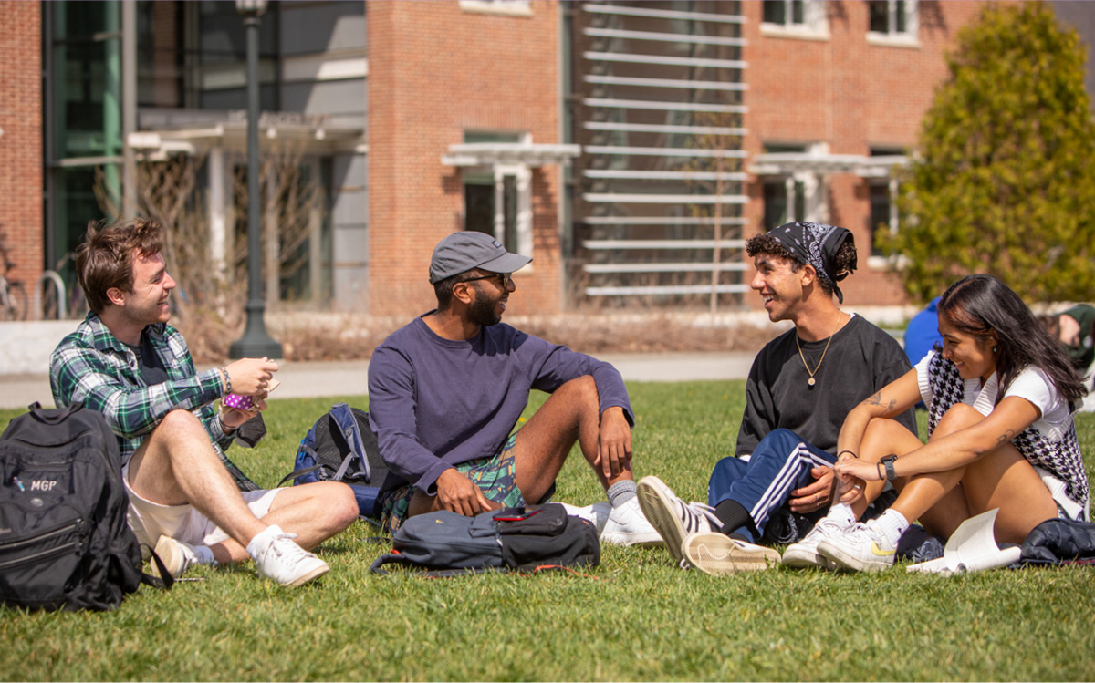 four students sitting on the quad smiling