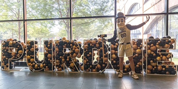 Purdue Pete stands next to balloons that spell PURDUE