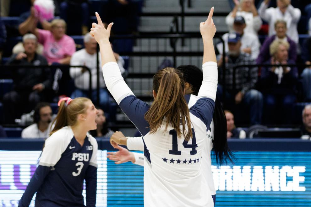 Women's volleyball player standing on court with arms up, facing the cheering crowd in the background. 