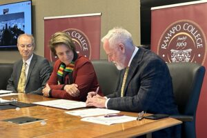 Three people sit behind a table to sign papers.